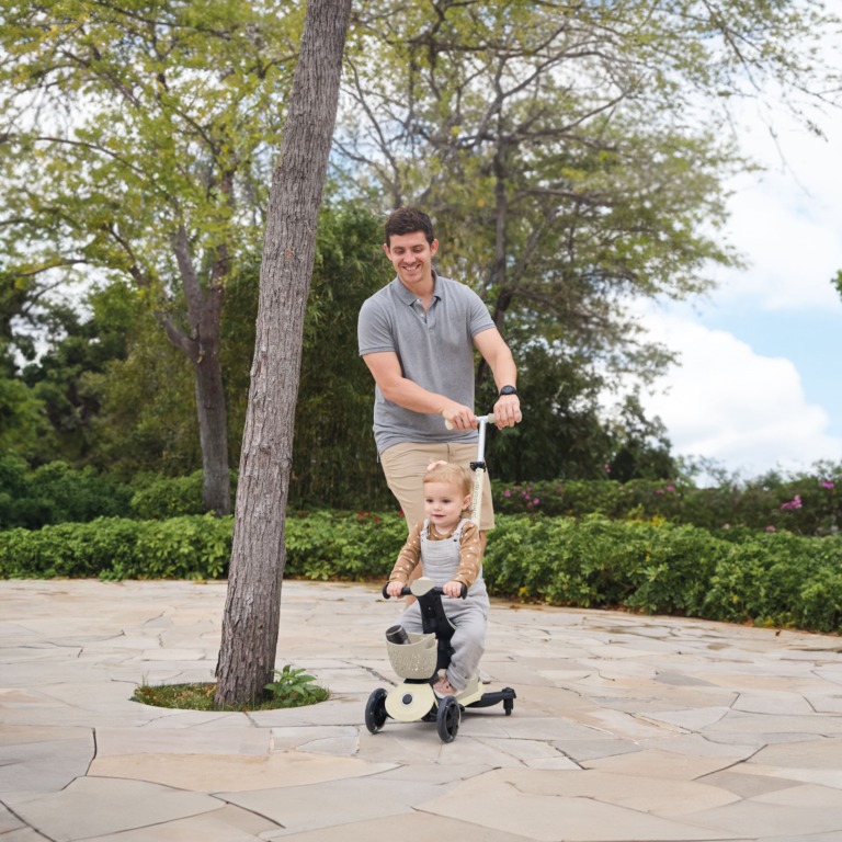 Niña en el Go Up Baby Luces 360 color taupe modo patinete guiado por su padre
